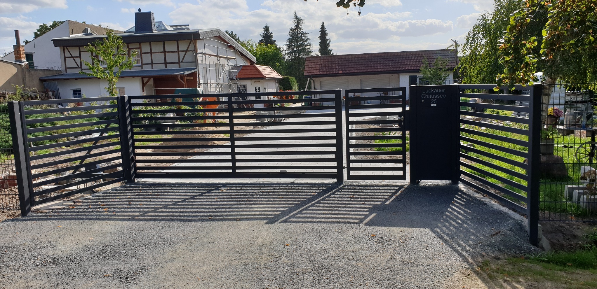Nowoczesna, pozioma brama wjazdowa z furtką w kolorze antracytowym, z adresem 'Luckauer Chaussee 25', prowadząca do posesji z domem w trakcie remontu.