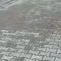 VERSA CORP SPÓŁKA Z OGRANICZONĄ ODPOWIEDZIALNOŚCIĄ - Szara kostka brukowa ułożona wzorem jodełki przy budynku. Widoczne delikatne zabrudzenia na powierzchni kostki. Ujęcie z niskiej perspektywy.