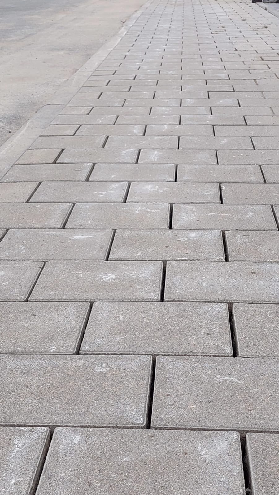 Szara kostka brukowa ułożona w regularny wzór, widok z perspektywy, z delikatnym cieniem podkreślającym fakturę. Minimalistyczny design chodnika.