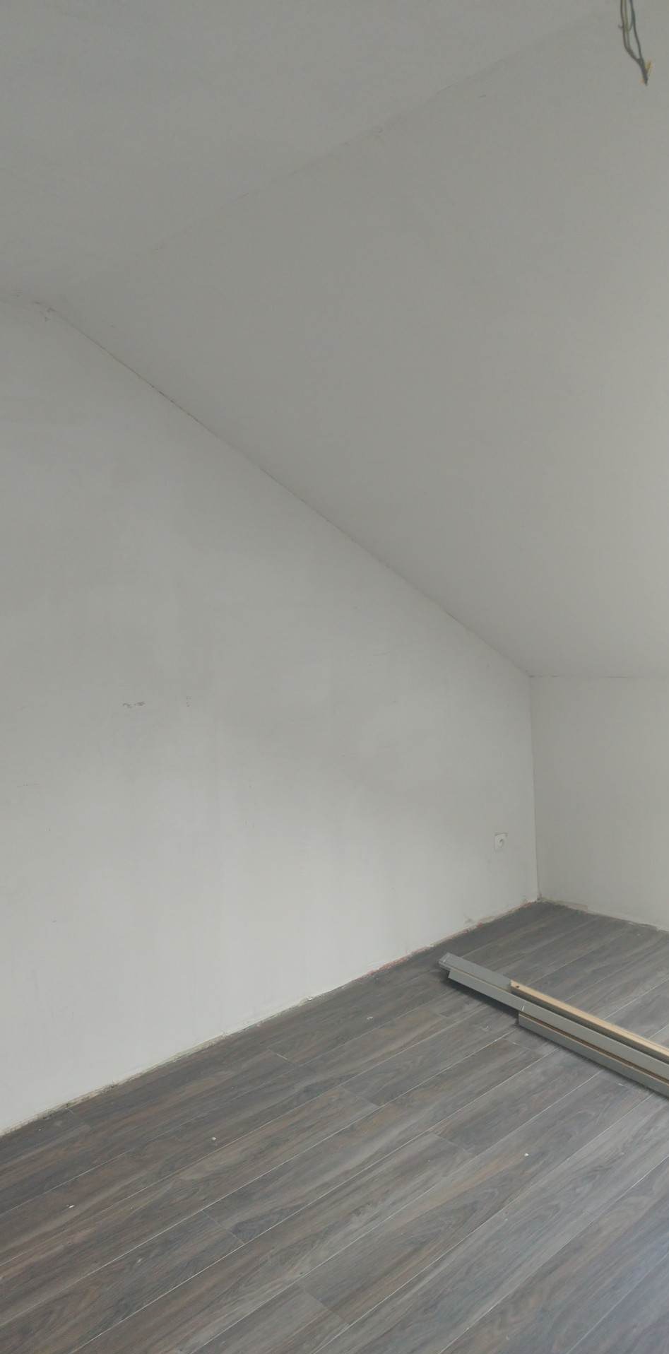 Poddasze po remoncie: szare panele podłogowe ułożone na skos, ściany pomalowane na biało, widoczne listwy przypodłogowe.
