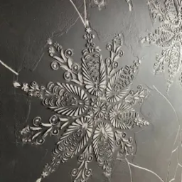 Szara ściana z dekoracyjnymi, wypukłymi wzorami w kształcie stylizowanych kwiatów i roślin, wykonana techniką strukturalną.