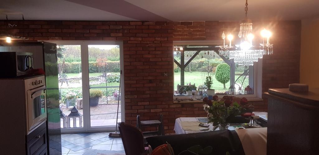 Ceglana ściana w pokoju z widokiem na ogród przez okno i drzwi balkonowe, kryształowy żyrandol.