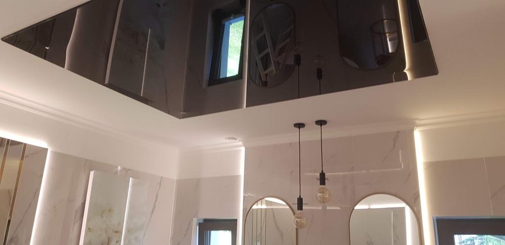 Nowoczesna łazienka z czarnym, lustrzanym sufitem podwieszanym, oświetleniem LED i dwoma wiszącymi lampami z żarówkami Edisona, odbicie okna w suficie.