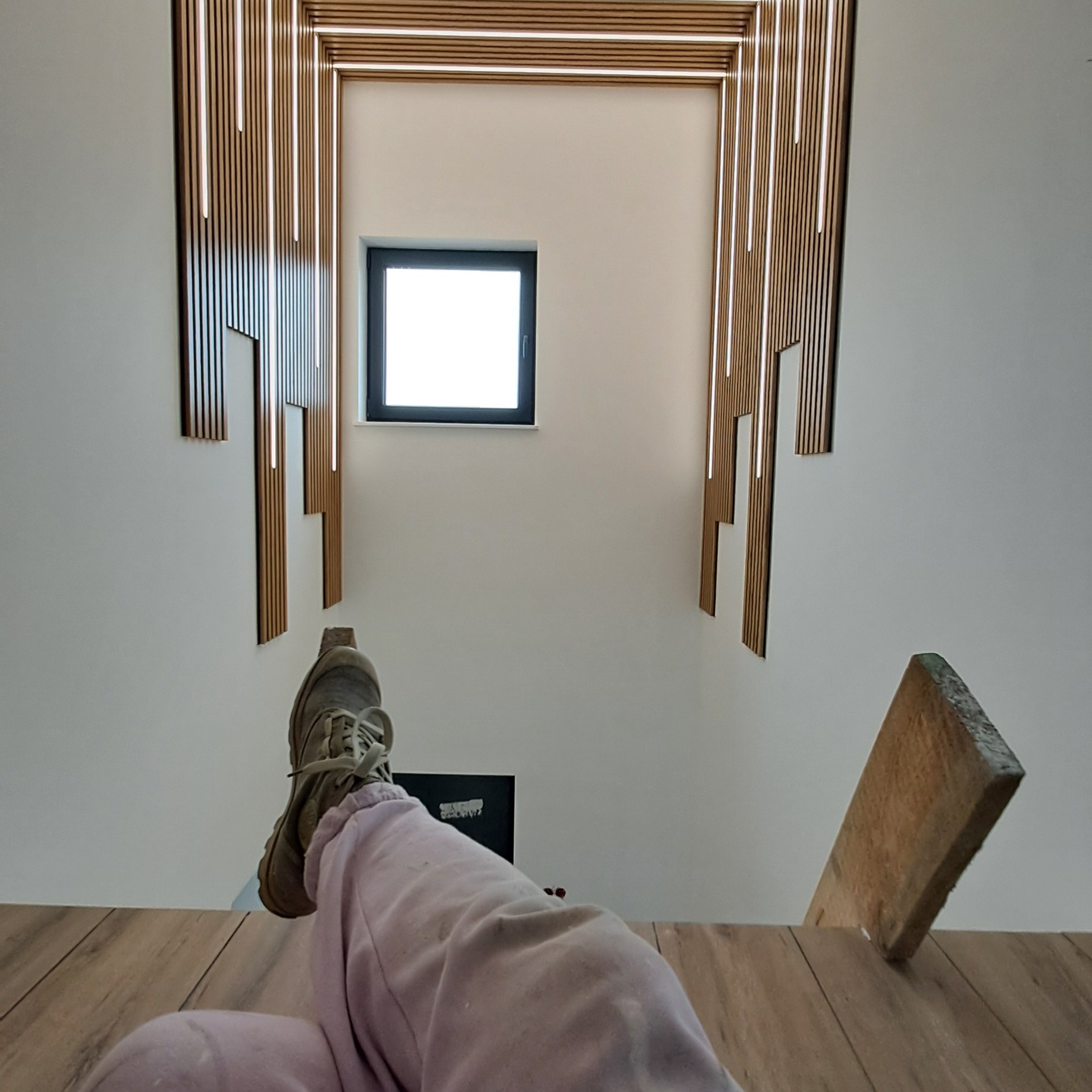 Nowoczesne wykończenie ścian z drewnianych paneli z wbudowanym oświetleniem LED, widok z dołu z fragmentem osoby w dresie i butach.