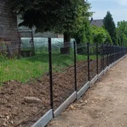 Czarny ogrodzenie panelowe z podmur&oacute;wką betonową, widok z zewnątrz posesji, w tle drzewa i dom.