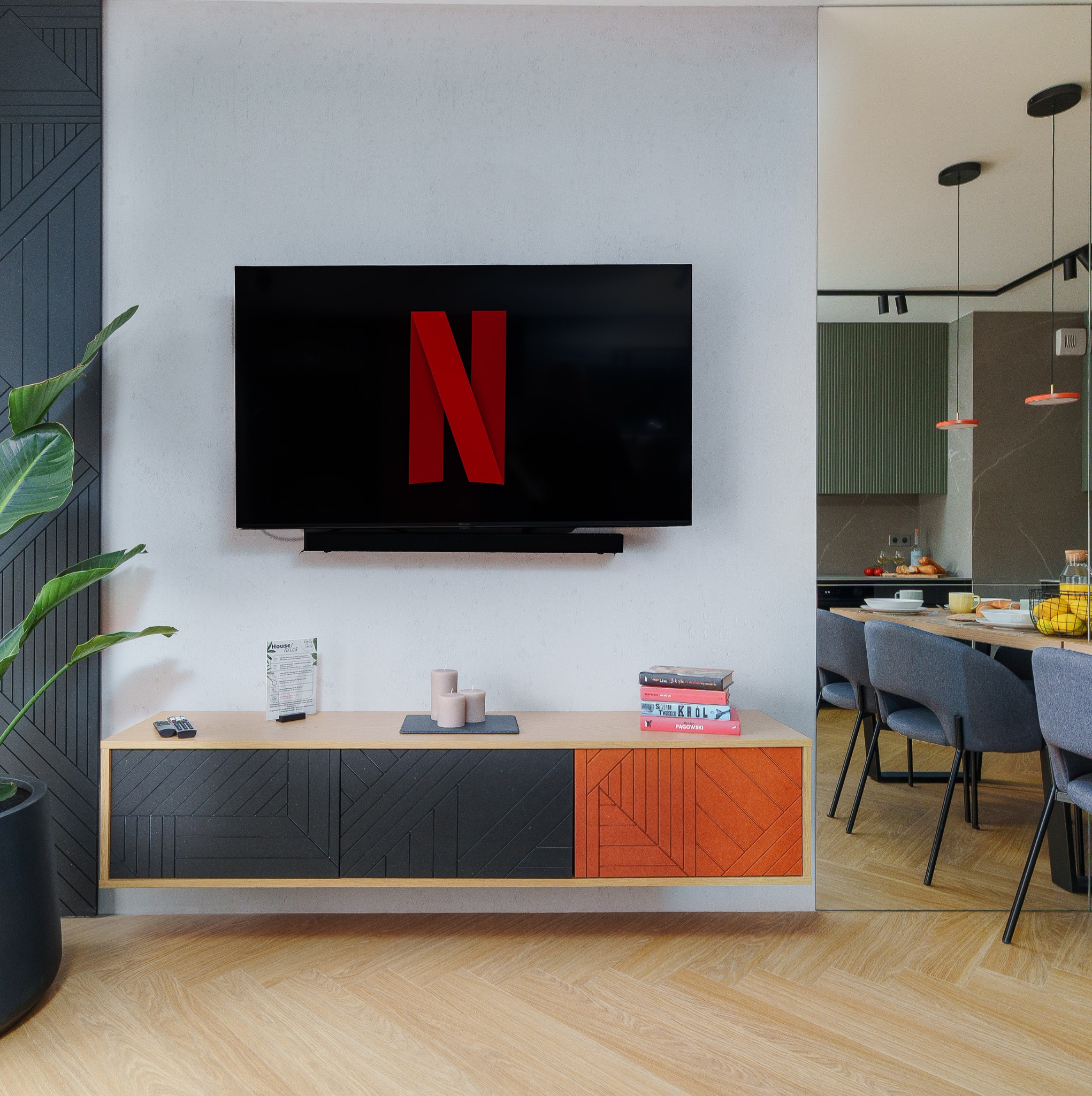 Nowoczesny salon z telewizorem z logo Netflix, szafką RTV z geometrycznym wzorem i parkietem w jodełkę. W tle widoczna jadalnia i kuchnia.