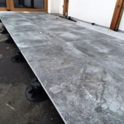 Montaż szarej, marmurkowej terakoty na regulowanych wspornikach tarasowych, widoczne narzędzia i poziomica, prace w toku.