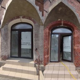 PUC MAJSTER - Porównanie stanu elewacji budynku przed i po renowacji, widoczne różnice w kolorze cegły i czystości fug, z otwartymi drzwiami wejściowymi z plakatem informującym o otwarciu salonu.