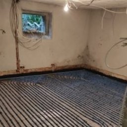 MAXIWIT SPÓŁKA Z OGRANICZONĄ ODPOWIEDZIALNOŚCIĄ - Ułożone rury ogrzewania podłogowego w surowym pomieszczeniu z oknem. Widoczne kable na ścianie i surowy beton. Etap prac przed wylaniem posadzki.