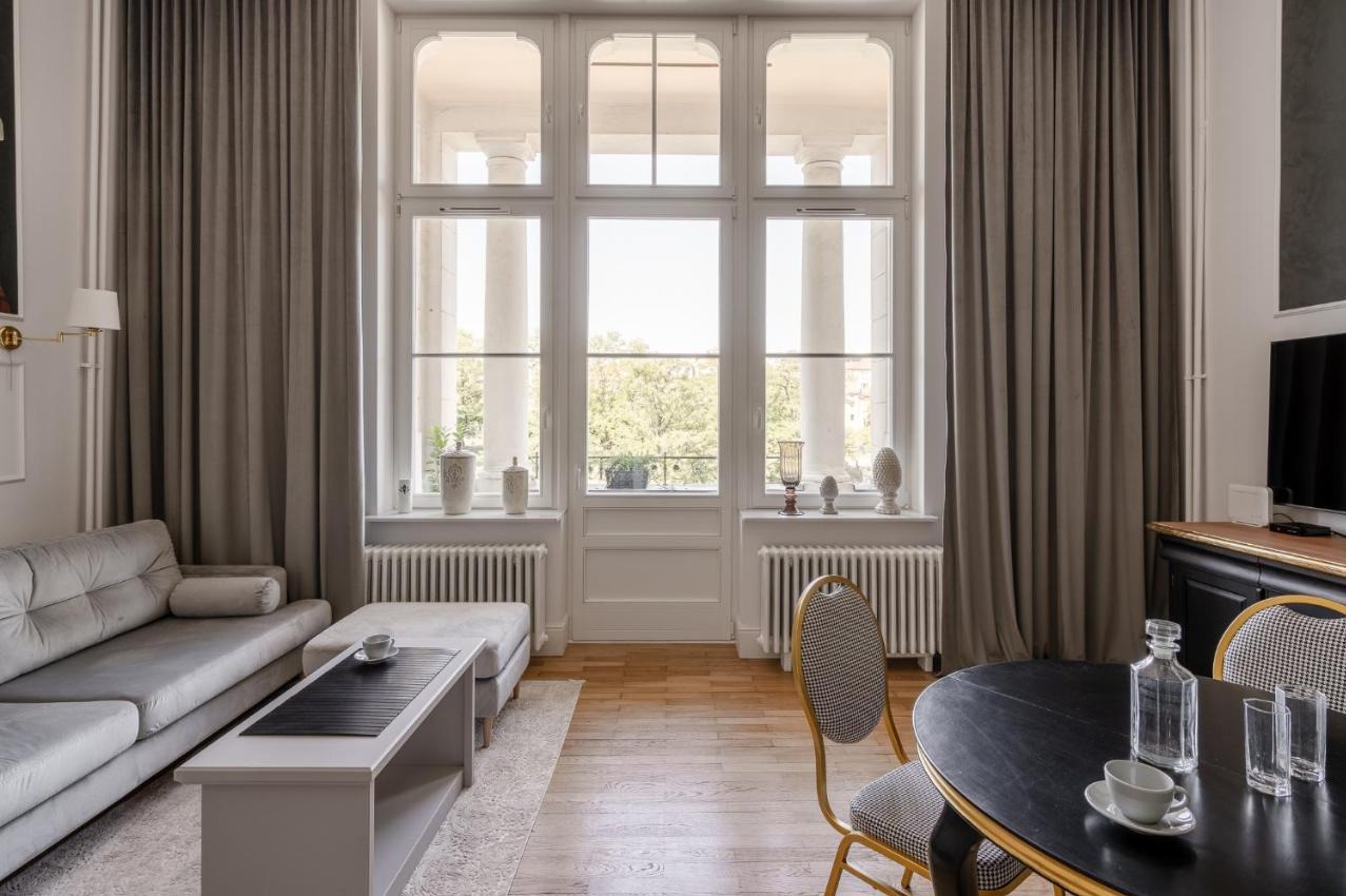 Eleganckie wnętrze salonu z dużym oknem kolumnowym, szarymi zasłonami, sofą, stolikiem kawowym, okrągłym stołem i parkietem w jodełkę.