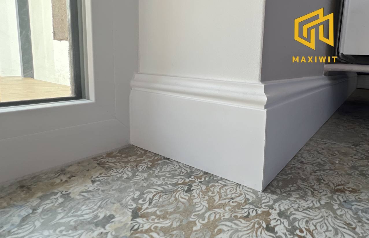 Białe listwy przypodłogowe po renowacji, zamontowane przy ścianie i oknie we Wrocławiu. Dekoracyjna podłoga z wzorem. Detal wykończenia wnętrza.