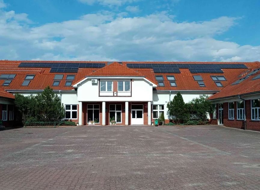 Budynek z czerwonym dachem, na którym zamontowano panele słoneczne, widok z dziedzińca.