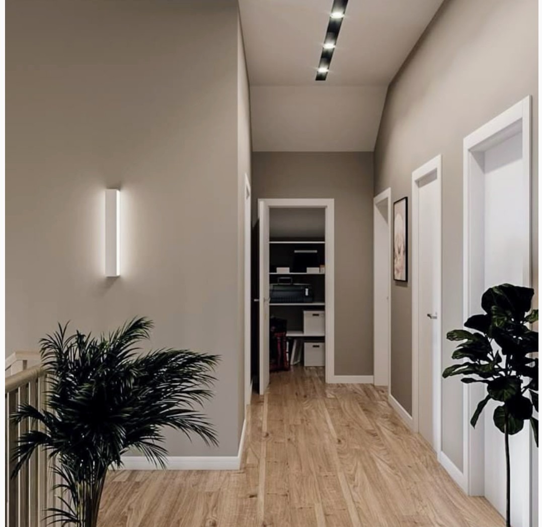 Nowoczesny korytarz z drewnianą podłogą, oświetleniem LED, roślinami doniczkowymi i ścianami w odcieniach beżu. Widok na otwartą garderobę.