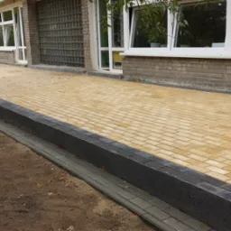 Nowo wyłożona, żółta kostka brukowa przed budynkiem z cegły, z widocznymi schodami i obrzeżami z ciemnej kostki.