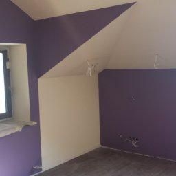 HARTMAN DM SPÓŁKA Z OGRANICZONĄ ODPOWIEDZIALNOŚCIĄ - Pokój po malowaniu w odcieniach fioletu i bieli, z widocznymi przewodami elektrycznymi wystającymi ze ścian i sufitu, okno zabezpieczone folią malarską.