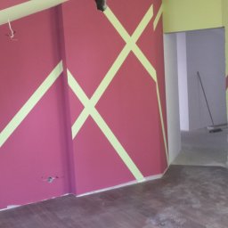 HARTMAN DM SPÓŁKA Z OGRANICZONĄ ODPOWIEDZIALNOŚCIĄ - Ściana w pokoju z geometrycznymi wzorami w kolorach różowym i jasnozielonym, widoczne gniazdka elektryczne i przewody, podłoga z paneli imitujących drewno, pomieszczenie w trakcie prac...