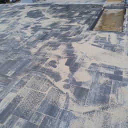 DARKABUD - Ułożona szara kostka brukowa z piaskiem w szczelinach, widoczny fragment studzienki rewizyjnej oraz materiały budowlane w tle.