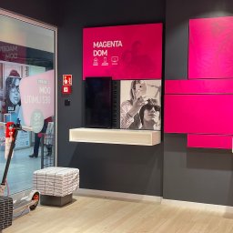 BMP Struzik Piotr - Wnętrze punktu obsługi klienta operatora telekomunikacyjnego z elementami identyfikacji wizualnej marki Magenta Dom, w tym plakaty i aranżacja przestrzeni.