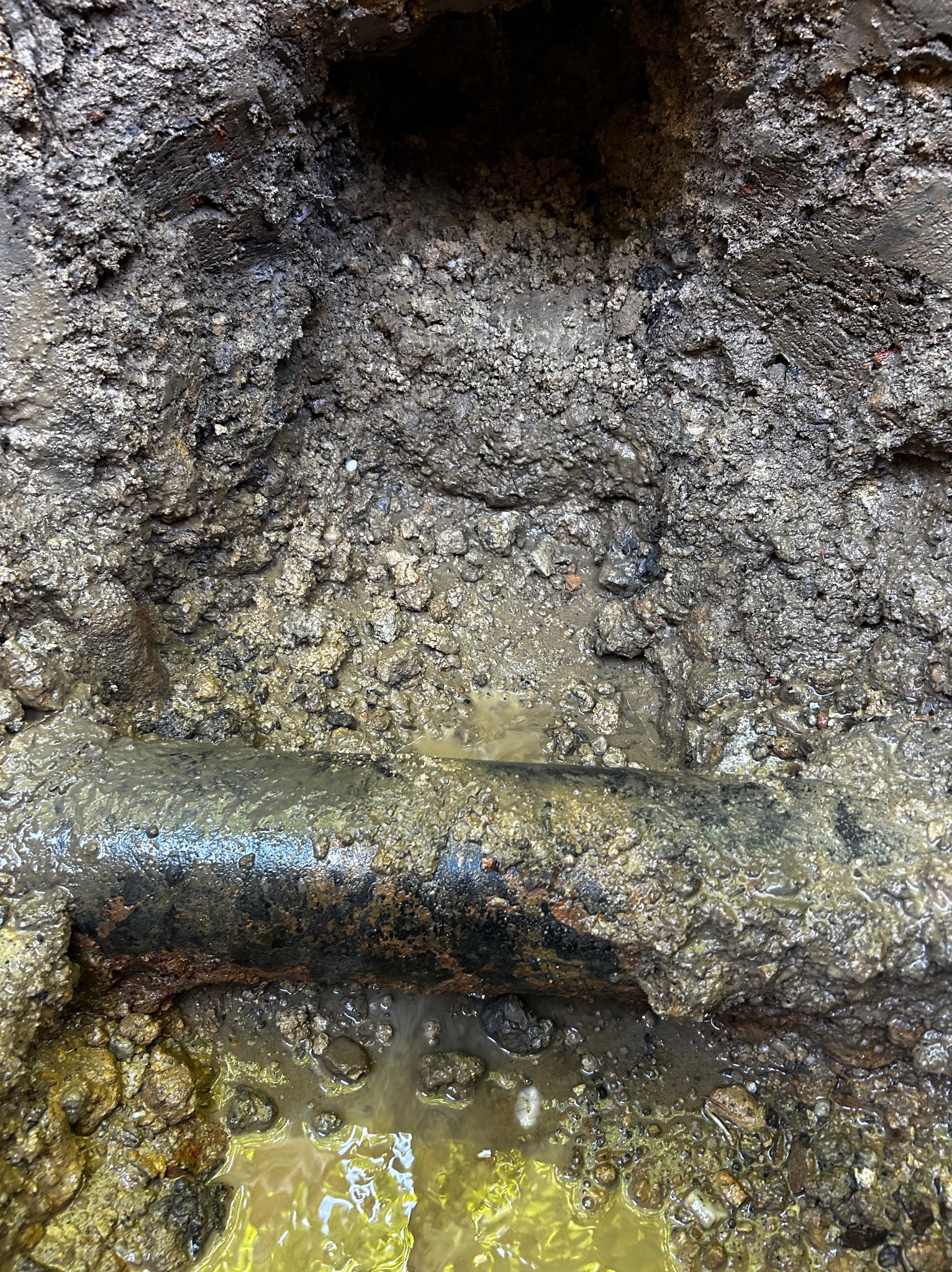 Odkopana, skorodowana rura wodociągowa w ziemi, widoczne ślady wycieku i mokra ziemia.