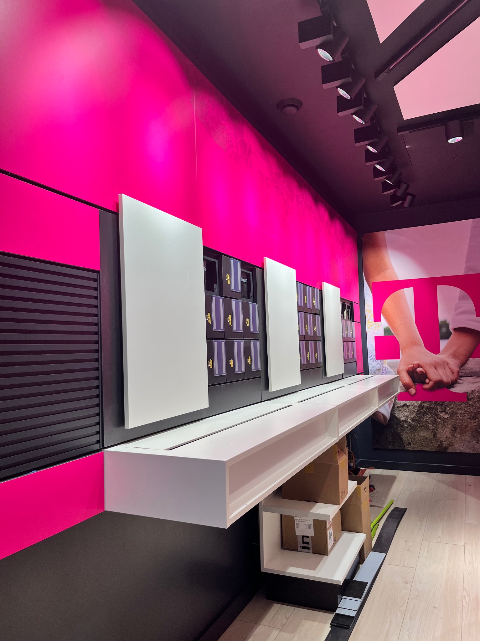 Nowoczesne wnętrze sklepu z intensywną różową ścianą, czarnymi elementami i białymi panelami, z widocznymi półkami na produkty i dużym plakatem reklamowym w tle.