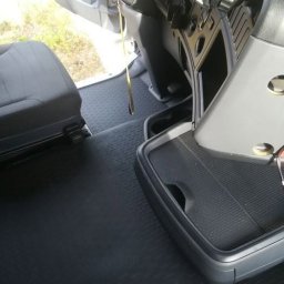 Mr. Glancer - Wnętrze kabiny pojazdu z gumową podłogą o fakturze kratki, widoczny fragment fotela, deski rozdzielczej z kluczykami i uchwyt na napoje.