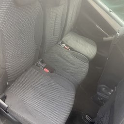 Mr. Glancer - Wnętrze samochodu z trzema szarymi fotelami z tkaniny o drobnej strukturze, widoczne pasy bezpieczeństwa i siatka na drobiazgi, po praniu tapicerki.