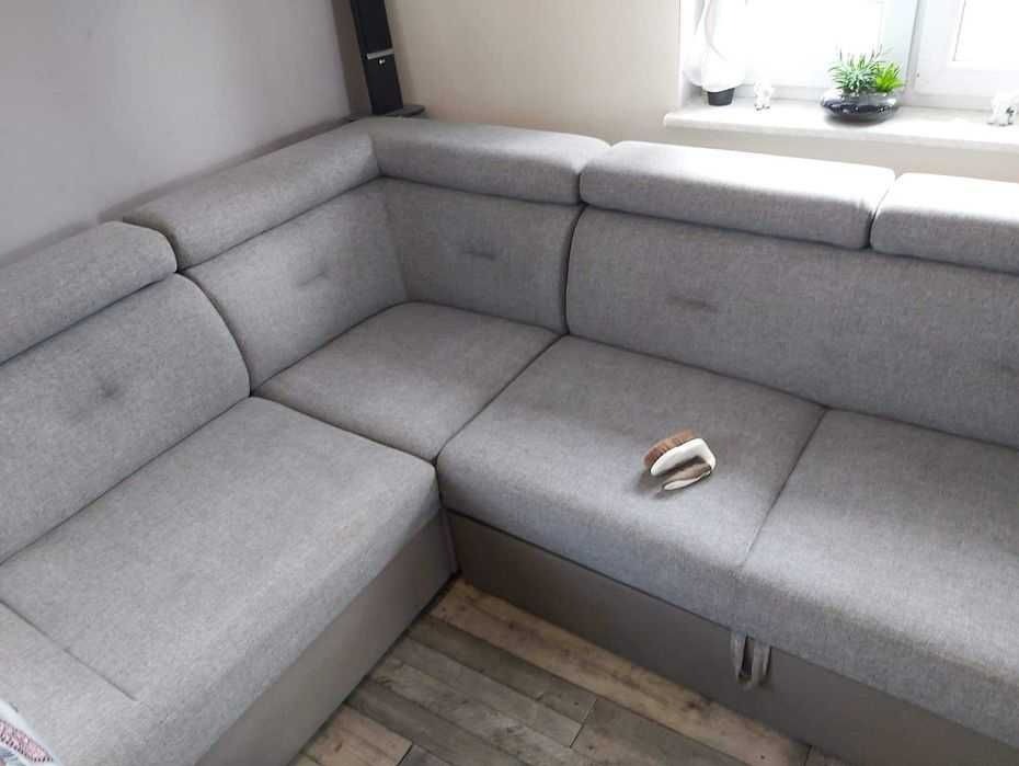 Szara, modułowa kanapa narożna z pojemnikiem na pościel, widoczna z boku, z poduszką dekoracyjną na jednym z siedzisk.