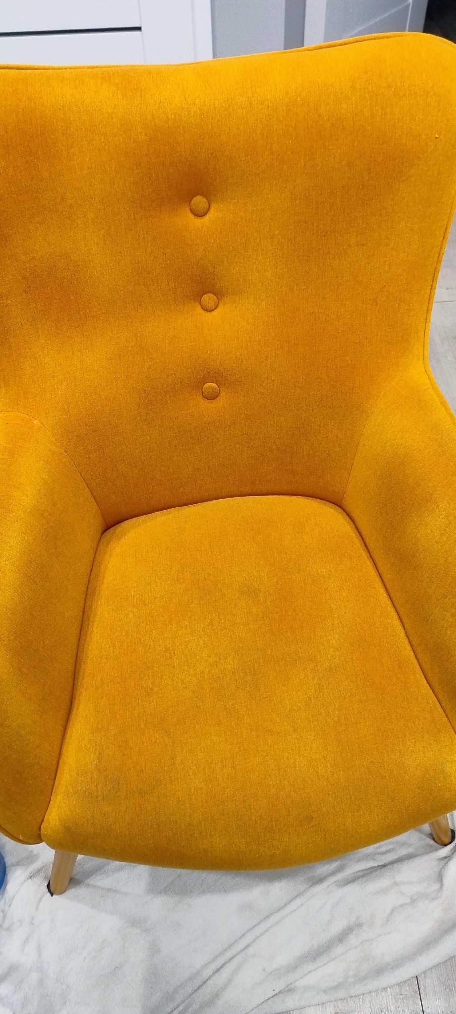 Żółty fotel tapicerowany z trzema guzikami na oparciu, częściowo zakryty białą szmatką ochronną.