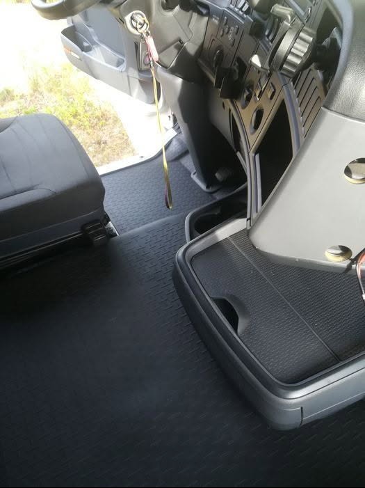 Wnętrze kabiny pojazdu z gumową podłogą o fakturze kratki, widoczny fragment fotela, deski rozdzielczej z kluczykami i uchwyt na napoje.