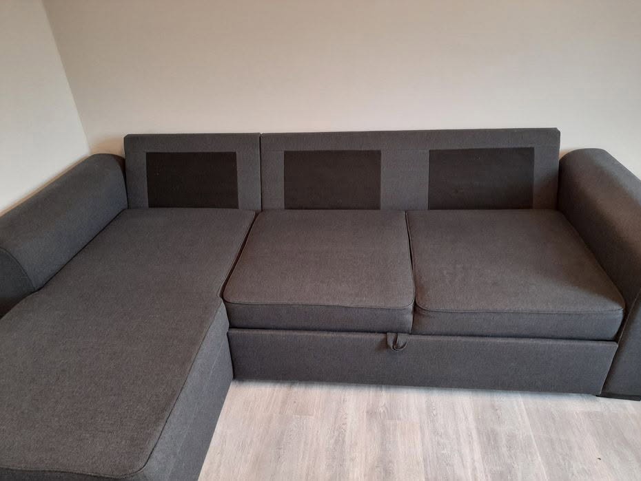 Rozłożona narożna kanapa w odcieniach szarości z ciemniejszymi wstawkami na oparciu, widoczny mechanizm wysuwania siedziska.