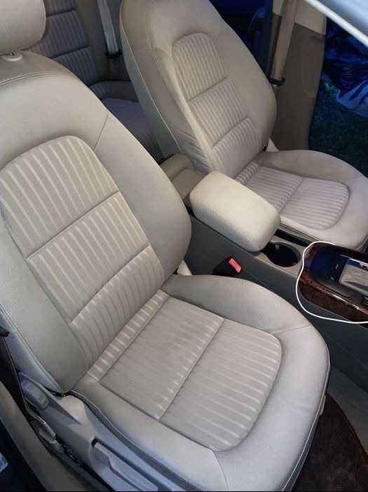 Jasnoszare, materiałowe fotele samochodowe z delikatnym wzorem w paski, widoczne po czyszczeniu, z detalami wnętrza auta w tle.