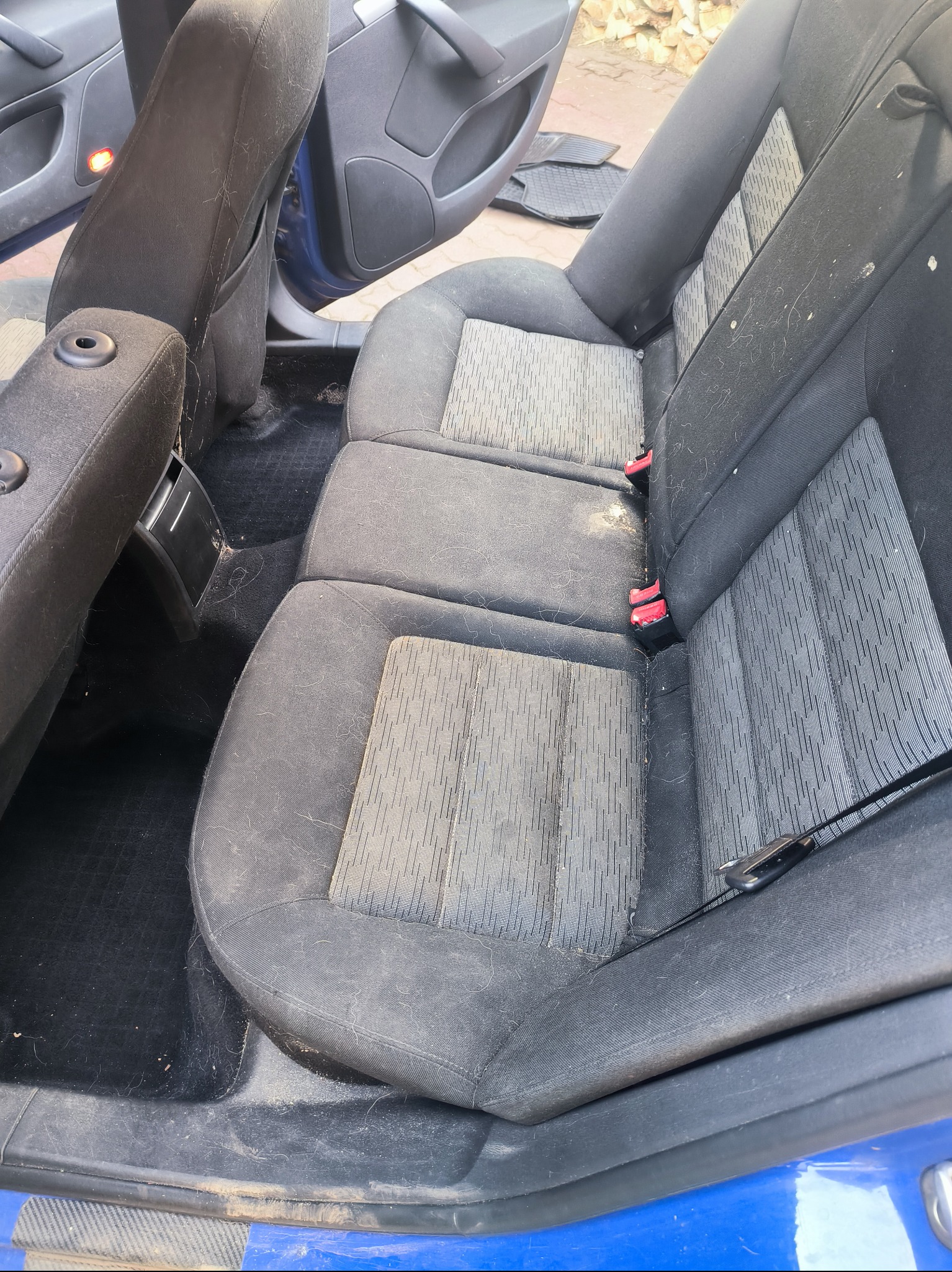 Silnie zabrudzona tylna kanapa w samochodzie koloru niebieskiego, widoczne plamy i sierść zwierząt na tapicerce oraz dywanikach.