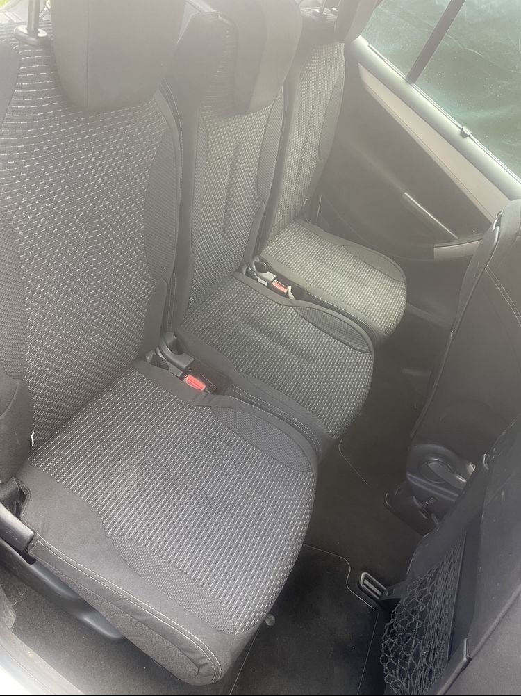 Wnętrze samochodu z trzema szarymi fotelami z tkaniny o drobnej strukturze, widoczne pasy bezpieczeństwa i siatka na drobiazgi, po praniu tapicerki.