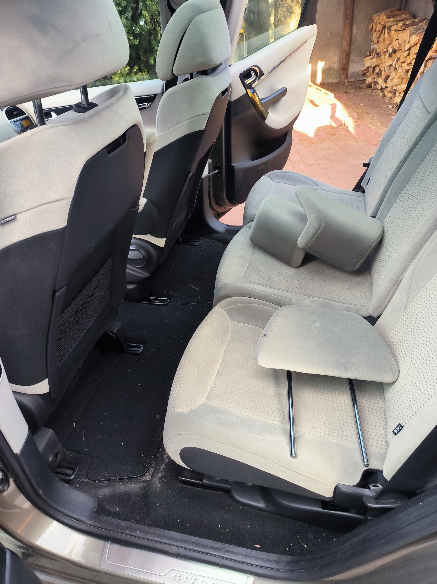 Wnętrze samochodu marki Citroen z widocznymi, jasnymi, materiałowymi siedzeniami tylnymi. Widoczne plamy i zabrudzenia na tapicerce oraz podłodze.