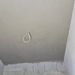 Firma Ogólnobudowlana Chwastyniak - Gładki, szary sufit po nałożeniu gładzi szpachlowej, z wiszącym przewodem elektrycznym, widok na surowe ściany z zabezpieczonymi otworami okiennymi.