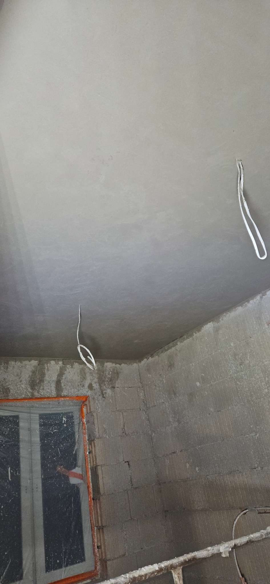 Wyrównany sufit w trakcie prac wykończeniowych w Śmigielu, widoczne wystające przewody elektryczne i fragment ściany z pustaków.