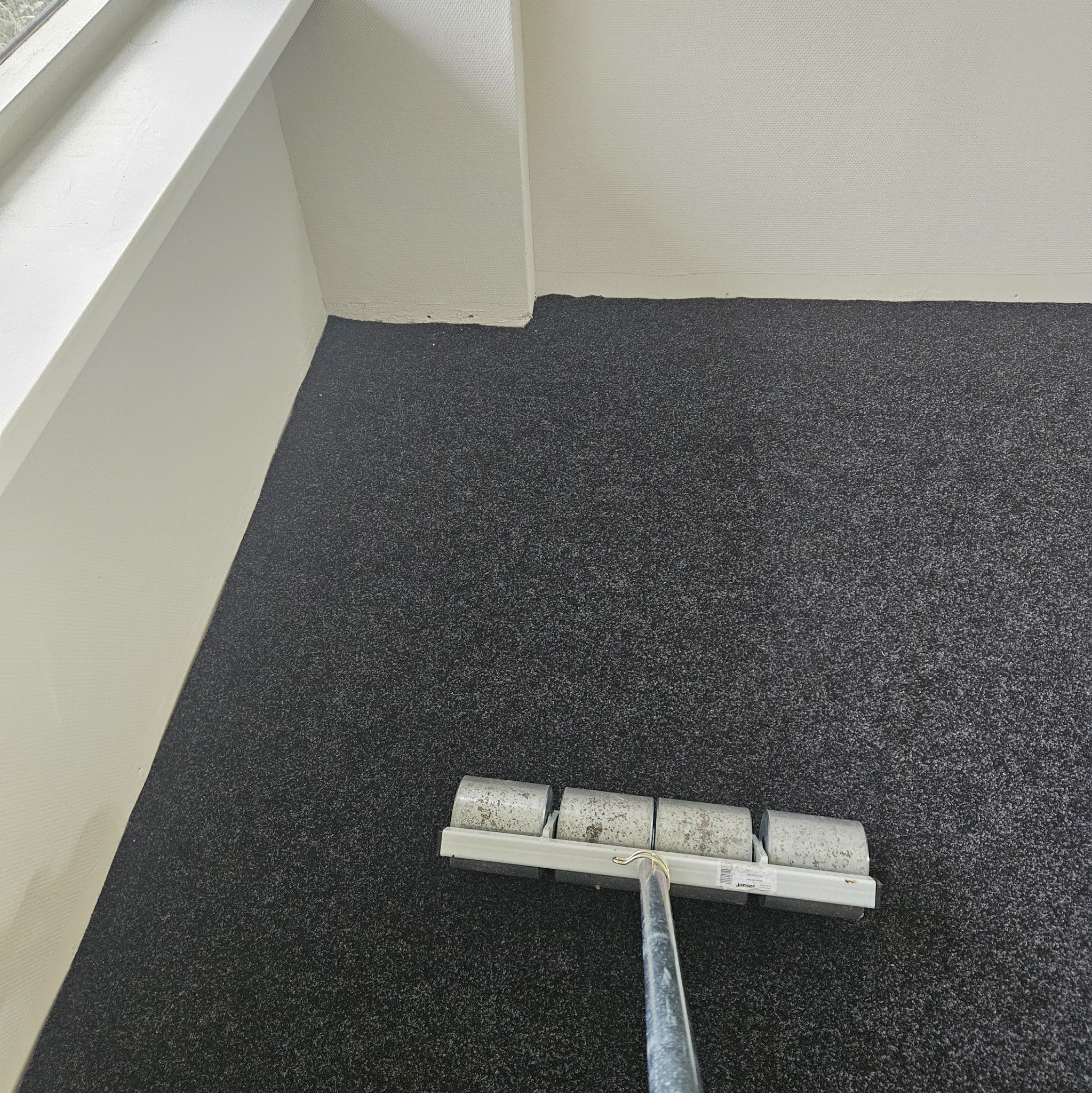 Wałek do tapetowania na ciemnoszarym, ziarnistym tle, prawdopodobnie ściany, blisko białej ściany i okna.