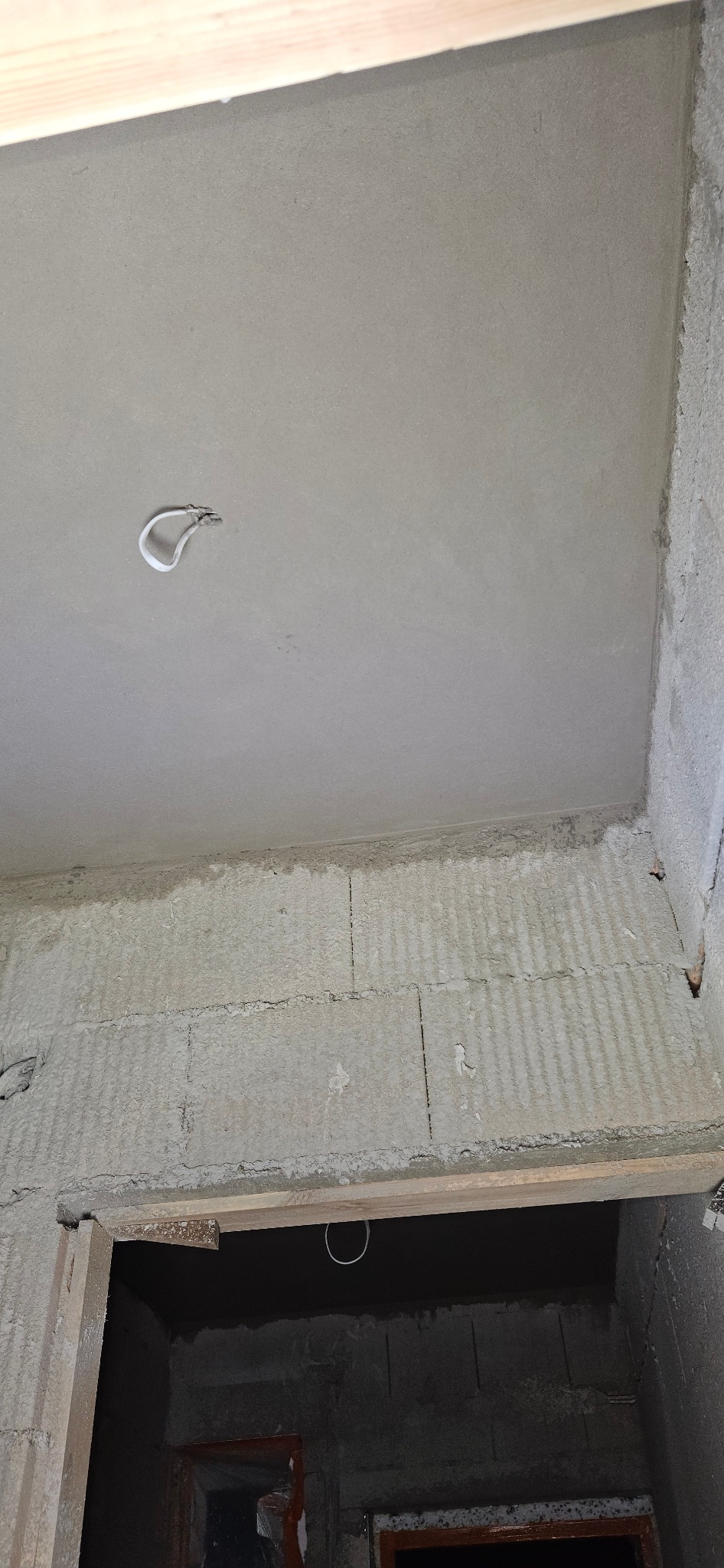 Surowy strop z widocznym kablem oświetleniowym i fragmentem ściany z pustaków, w tle otwór drzwiowy, etap prac wykończeniowych.