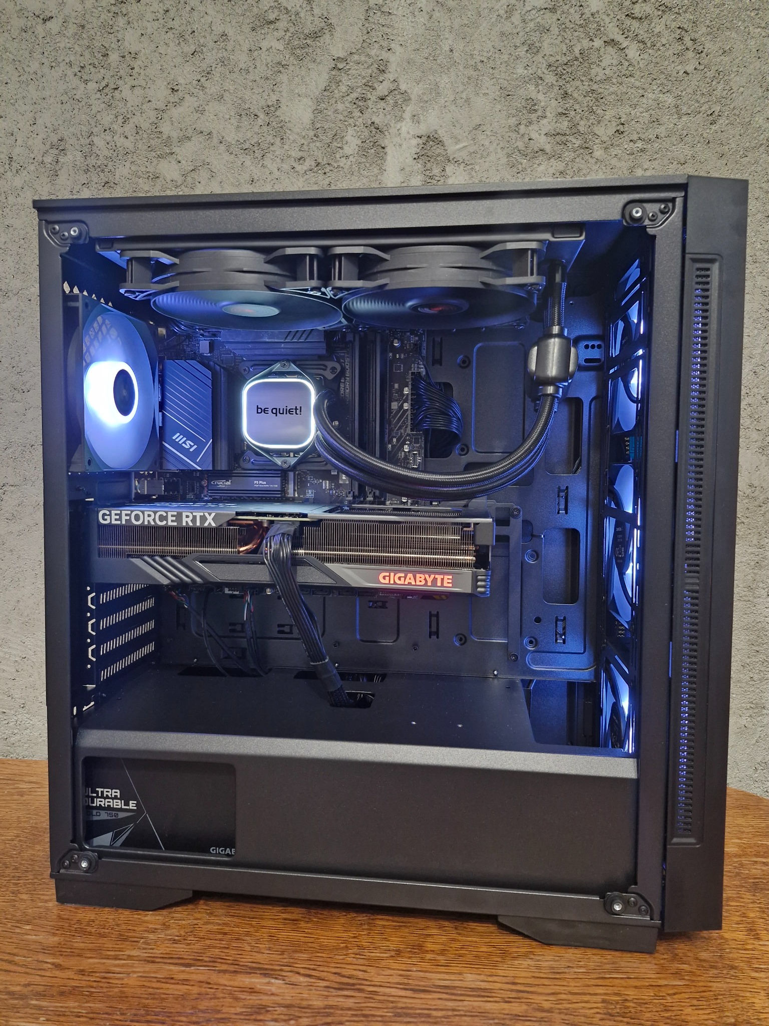 Wnętrze złożonego komputera stacjonarnego z kartą graficzną GeForce RTX, chłodzeniem wodnym Be Quiet, wentylatorami MSI z podświetleniem LED i pamięcią Crucial, widoczne kable i komponenty...