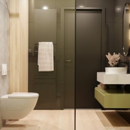 NAVRO. - Studio Projektowe - mgr inż. arch. Piotr Nawrocki - Nowoczesna łazienka z betonową ścianą, drewnianą okładziną, wiszącą toaletą, kabiną prysznicową z ręcznikiem, umywalką na marmurowym blacie z zieloną szafką i owalnym lustrem z oświetleniem.