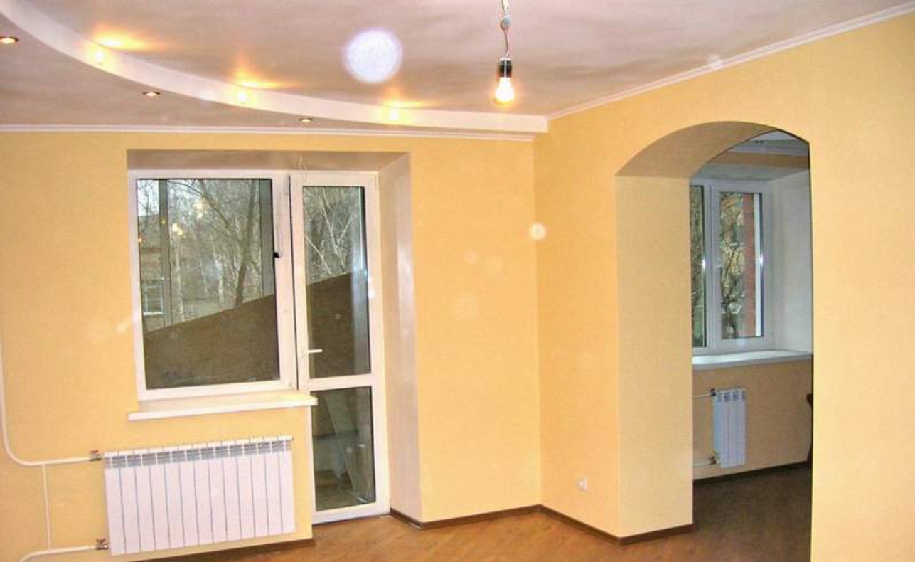 Jasne wnętrze po remoncie w Gdańsku: żółte ściany, białe okna z grzejnikami. Widoczny łuk między pokojami i podwieszany sufit z oświetleniem.