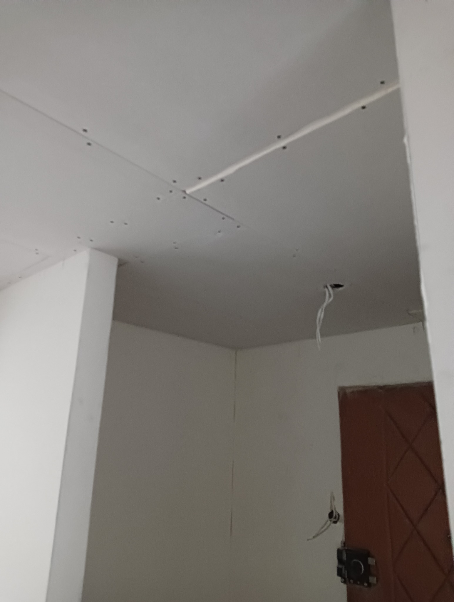 Płyty gipsowo-kartonowe zamontowane na suficie, widoczne śruby mocujące, wystające przewody elektryczne, fragment ściany z ościeżnicą.