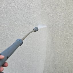 Puc Majster Małopolska - Czyszczenie elewacji jasnym strumieniem wody pod ciśnieniem, widoczny fragment elewacji przed i po czyszczeniu, w tle drobne kamienie