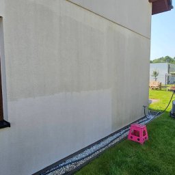 Puc Majster Małopolska - Fragment elewacji budynku z widoczną różnicą w czystości po częściowym umyciu, brązowa roleta okienna, myjka ciśnieniowa Karcher, różowy stołek na trawie.