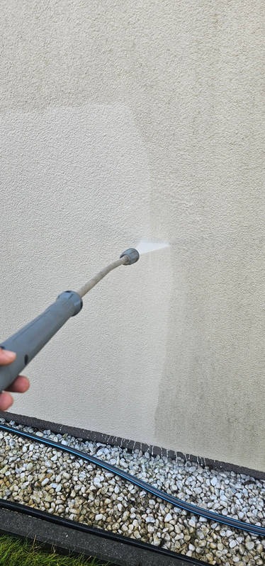 Czyszczenie elewacji jasnym strumieniem wody pod ciśnieniem, widoczny fragment elewacji przed i po czyszczeniu, w tle drobne kamienie