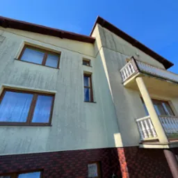 Brudna elewacja dwupiętrowego domu z balkonem w Pniewach, widziana z dołu pod kątem, przed czyszczeniem.