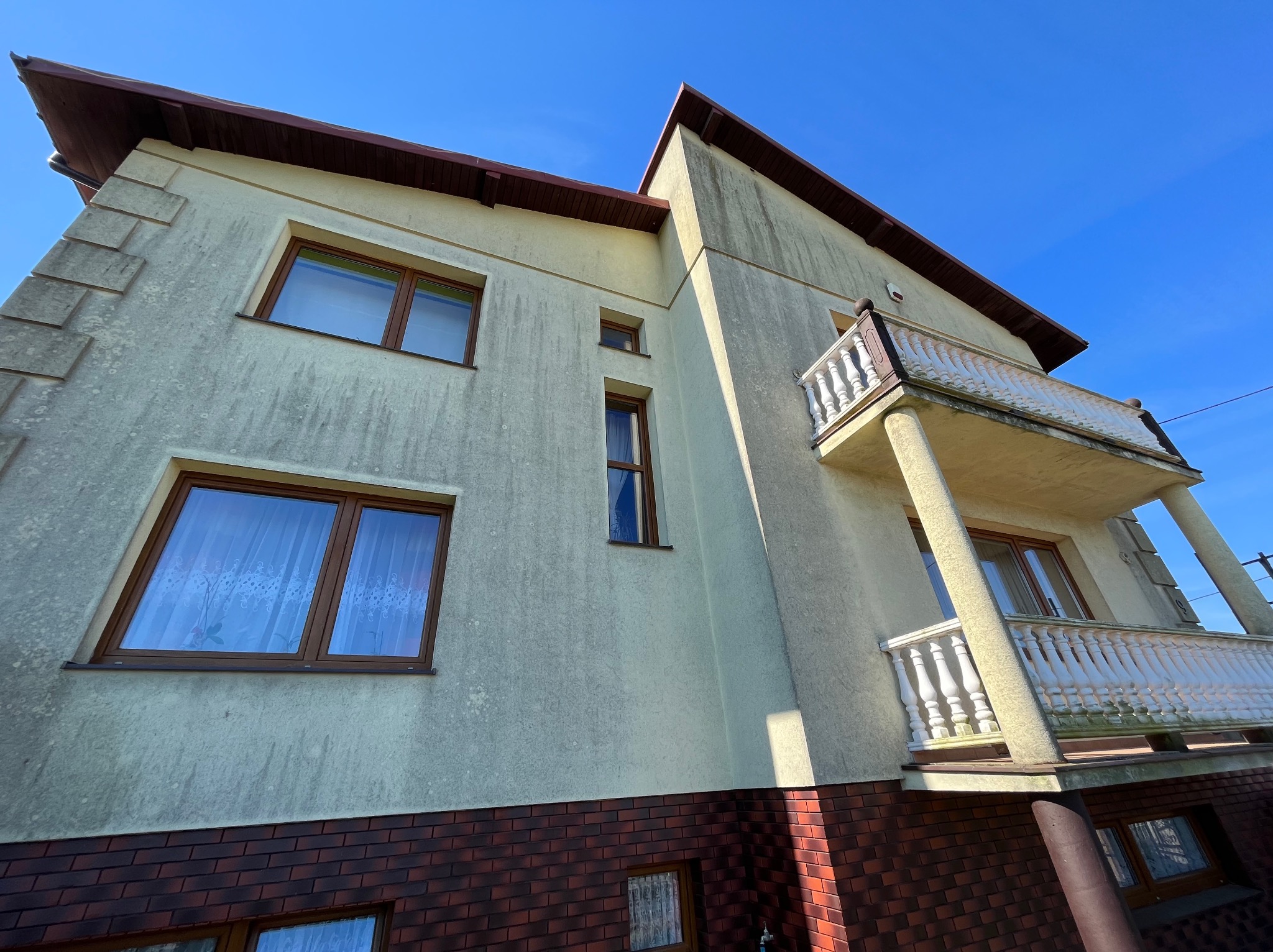 Brudna elewacja dwupiętrowego domu z balkonem w Pniewach, widziana z dołu pod kątem, przed czyszczeniem.
