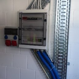 AMPERA POLSKA SPÓŁKA Z OGRANICZONĄ ODPOWIEDZIALNOŚCIĄ - Rozdzielnica elektryczna natynkowa z zabezpieczeniami, gniazda siłowe na ścianie z bloczków, koryta kablowe z przewodami w peszlach ochronnych.