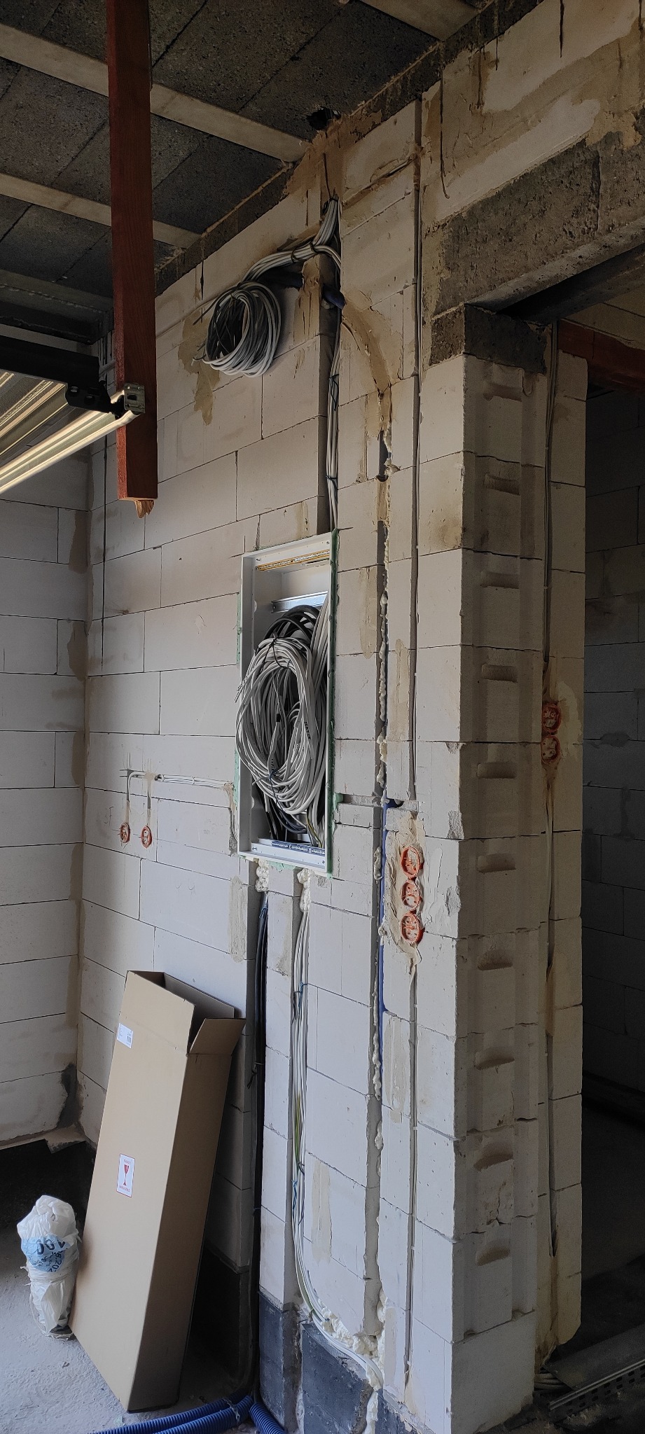 Wnętrze w trakcie prac wykończeniowych, widoczne przewody elektryczne w puszce podtynkowej i bruzdach w ścianie z betonu komórkowego, zabezpieczone pianką montażową, z fragmentem instalacji bramy...