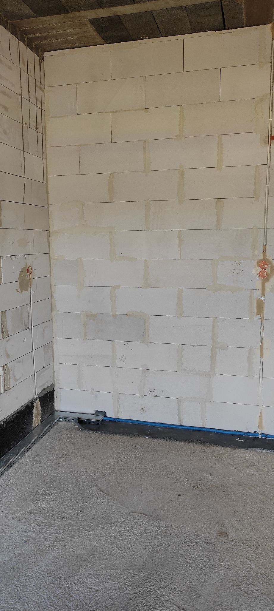 Surowy stan wnętrza z murem z betonu komórkowego, instalacją elektryczną w peszlu i wylewką podłogową w trakcie schnięcia.